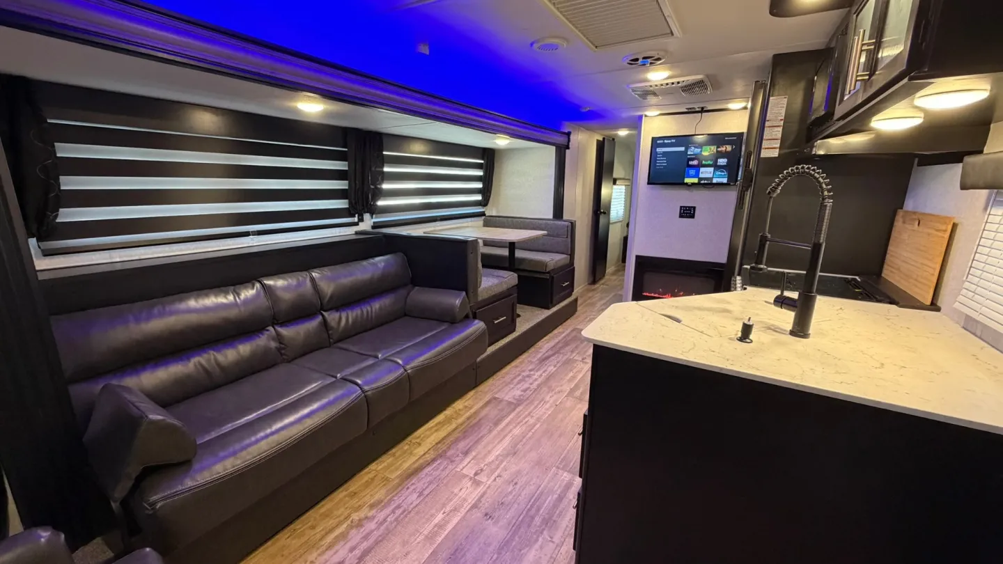 Inside a 1st Choice Living travel trailer: a sofa, dinette, wall TV, fireplace, and a kitchen island with a stone counter